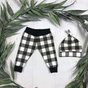 May include: Black and white checked baby leggings and hat set. The leggings have a black waistband and the hat has a knotted top.