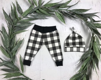 May include: Black and white checkered baby leggings and hat set. The leggings have a black waistband and the hat has a knotted top.