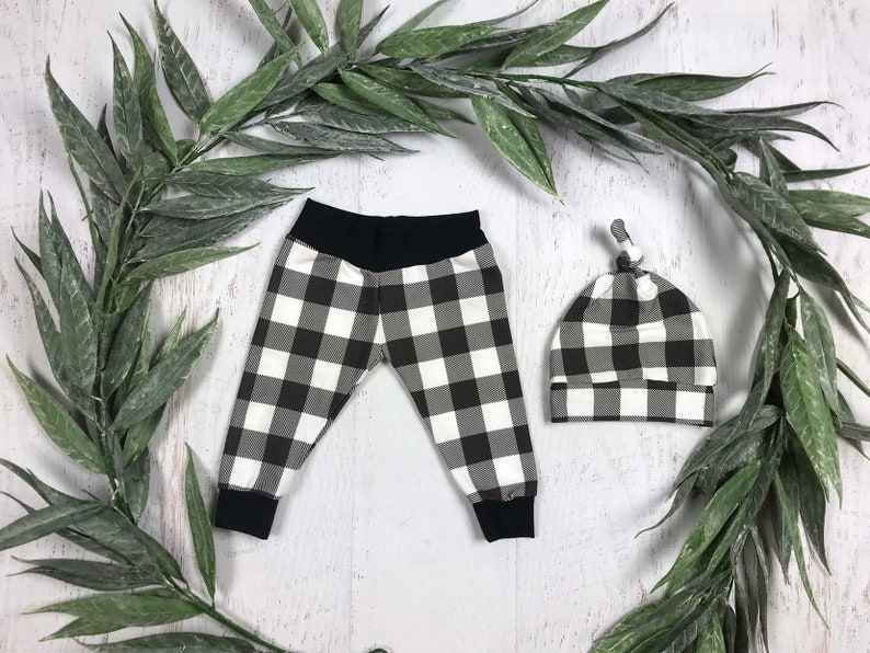 May include: Black and white checked baby leggings and hat set. The leggings have a black waistband and the hat has a knotted top.