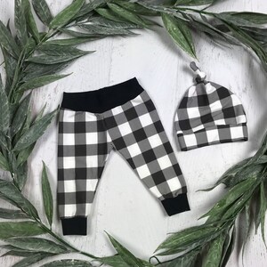 May include: Black and white checked baby leggings and a matching hat. The leggings have a black waistband and the hat has a knotted top.