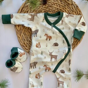 May include: A white baby onesie with a green trim and a woodland animal print. The onesie has a crossover front and is made of soft, comfortable fabric. The onesie is paired with matching green and brown booties.