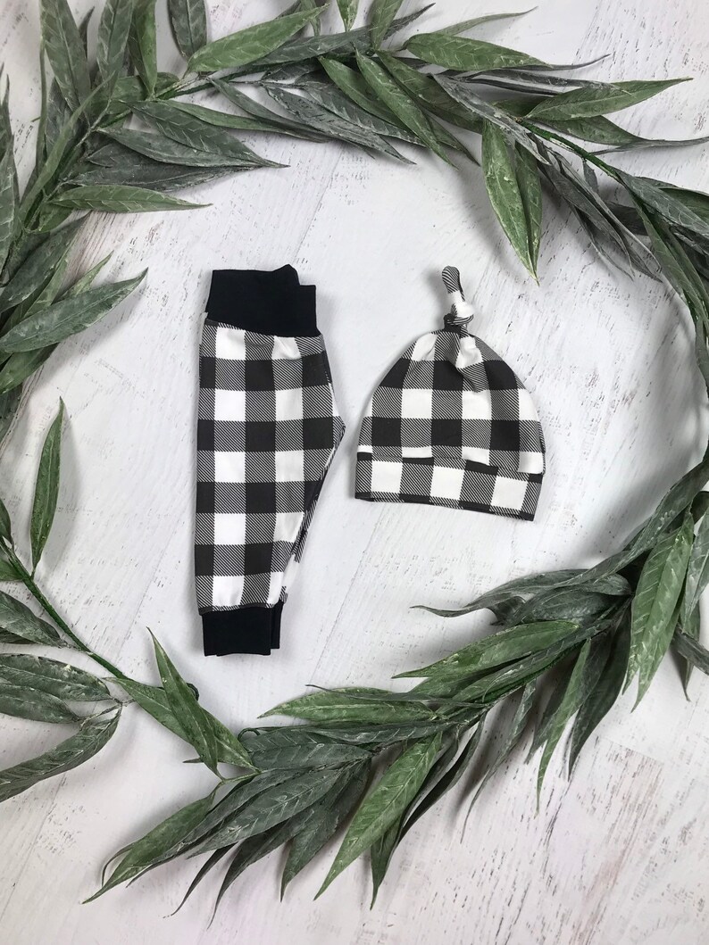 May include: Black and white checked baby trousers and hat set. The trousers have a black elastic waistband and the hat has a knotted top.