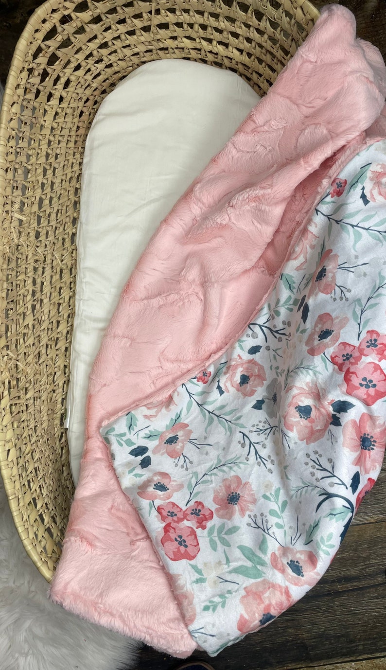 May include: A pink and white baby blanket with a floral pattern. The blanket is made of soft, plush fabric and is perfect for cuddling.