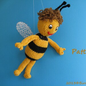 May include: A knitted bee toy with yellow and black stripes, brown hair, and white wings. The bee is hanging from a string against a blue background. The text "Pattern" is written in orange on the right side of the image.