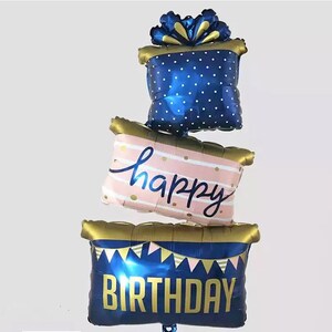 May include: A blue and gold balloon set with the words "happy birthday" in a pink and white striped balloon. The balloons are shaped like a gift box, a banner, and a pillow.