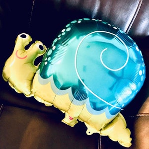 May include: A blue and yellow inflatable snail balloon with a smiling face. The snail is curled up in a spiral shape.