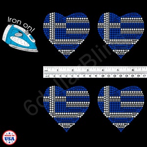 May include: Four heart-shaped iron-on rhinestone transfers featuring the Greek flag design in blue and white crystals. A blue and white iron graphic with the text "iron on!" is included. A ruler shows the width is approximately 6.5 inches.