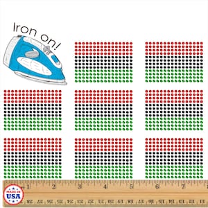 May include: Nine iron-on patches with red, black, and green dot patterns, resembling a flag design. A blue iron with the text "Iron on!" is in the upper left corner. A wooden ruler shows inches.