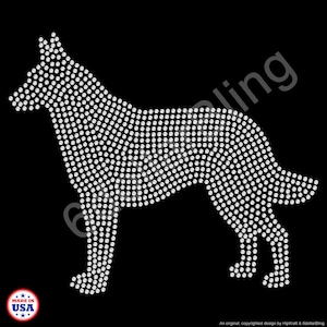 May include: A rhinestone design of a dog in a standing pose, composed of numerous small, round, white rhinestones. The dog silhouette is set against a black background. The words "MADE IN USA" are in a circle at the bottom left.