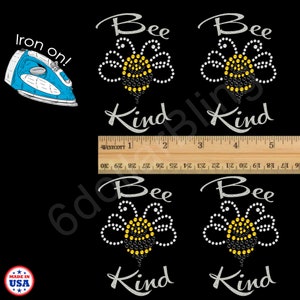 May include: Black background with four rhinestone "Bee Kind" designs. Each design features a bee with a yellow body and white wings. The text "Bee" and "Kind" are in a cursive font. An iron and a ruler are also in the image.
