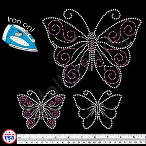 May include: Three butterfly iron-on rhinestone designs in white and pink, with a blue iron and the text "Iron on!" on a black background. The designs vary in size, with a ruler at the bottom showing inches.