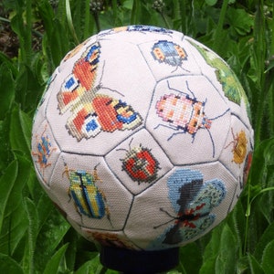 May include: A white football with a stitched design featuring various embroidered insects and butterflies. The insects include ladybugs, butterflies, and beetles in shades of red, blue, green, yellow, and pink.