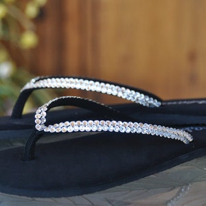 May include: Black flip-flops with a double row of clear rhinestones on the straps.