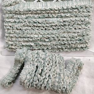 May include: Seafoam green and white decorative trim with a textured, looped design and a scalloped edge. A rolled section of the trim is also visible. The trim is suitable for various craft projects.