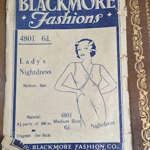 Op de afbeelding: Vintage Blackmore Fashions nachtjaponpatroon. Het blauw-witte papieren patroon toont de tekst "BLACKMORE Fashions" en een illustratie van een vrouw in een nachtjapon. Het patroon bevat afmetingen en materiaaleisen.
