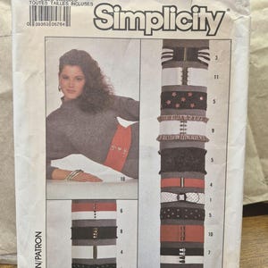 May include: A Simplicity sewing pattern envelope 8716 for various belts. The front shows a person wearing a wide red belt and displays illustrations of twelve different belt styles in black, white, and red with various buckles and closures.