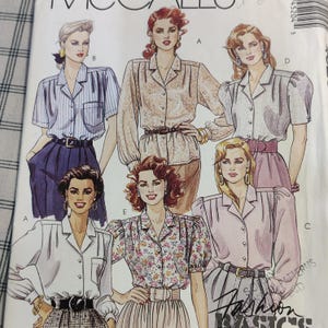 Op de afbeelding: Een naaipatroon met vijf verschillende blouse-ontwerpen. De blouses zijn allemaal in verschillende tinten wit, roze en blauw met verschillende mouw- en kraagstijlen. Het patroon is getiteld "Fashion Basics" en bevat instructies voor het maken van de blouses.
