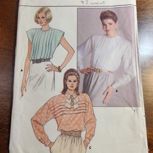 Puede incluir: Un patrón de costura Butterick vintage con ilustraciones de tres blusas. El patrón incluye tallas 8-10-12 y está marcado como sin cortar. Las blusas son de varios estilos, incluyendo un top plisado y una blusa de lunares.