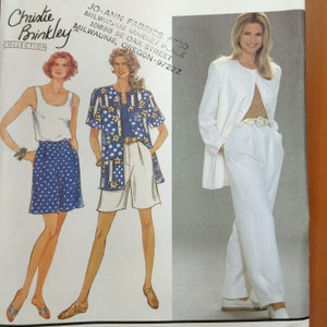 May include: A vintage fashion magazine page featuring the Christie Brinkley Collection. The page showcases illustrations of women's clothing, including a white tank top and blue polka dot skirt, a blue patterned jacket, and a white pantsuit.