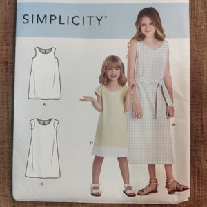 May include: A Simplicity sewing pattern featuring illustrations of children's dresses. The pattern includes diagrams of sleeveless and cap-sleeved dress designs. The image also shows two girls wearing dresses, one in a light yellow dress with a white hem and the other in a gingham dress.