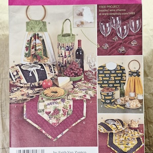 May include: A Simplicity sewing pattern envelope 1483 featuring instructions for kitchen and dining accessories. The cover displays images of wine-themed fabric projects like a towel, wine bottle bag, and table runner, alongside Green Bay Packers themed items.