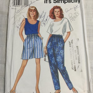 May include: A vintage sewing pattern package featuring illustrations of two women in different outfits. One model wears a blue tank top and striped shorts, the other a white top and floral pants. The package reads "it's Simplicity".