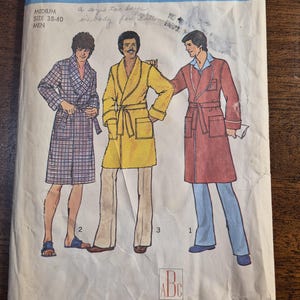 Könnte beinhalten: Vintage Simplicity Schnittmuster 7080 für Herren-Bademäntel. Das Muster zeigt Illustrationen von drei verschiedenen Bademantel-Stilen in verschiedenen Farben und Mustern. Enthält Transfers für Alphabet-Stickerei in zwei Größen.
