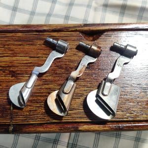 May include: Three silver sewing machine attachments with different sized circular ends and a curved handle. The attachments are labeled with the numbers 6, 9, and 4.
