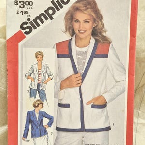 Puede incluir: Un sobre de patrón de costura Simplicity 5366 para un blazer de talla N. La portada muestra un blazer blanco con un panel rojo en el hombro y ribete azul, junto con dos ilustraciones más pequeñas que muestran variaciones del diseño.