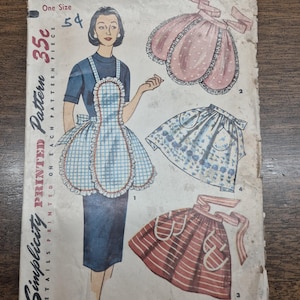 May include: Vintage Simplicity printed pattern envelope featuring apron designs. The envelope shows a woman wearing an apron with a blue and white checkered pattern. Other apron designs include a pink polka dot and a red striped apron.