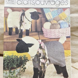 May include: Simplicity 7418 sewing pattern for stuffed sheep. The envelope features two sheep figures: one with white fur and black legs, and another wearing a black and white houndstooth coat with pink floral accents and ribbons.