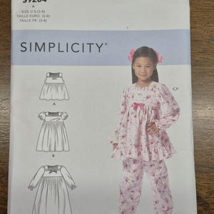 Puede incluir: Patrón de costura Simplicity S9204 para ropa de dormir infantil. El patrón incluye diagramas de diferentes estilos de ropa de dormir. La imagen también muestra a una niña pequeña con un conjunto de pijama floral rosa. Talla FR 3-8.