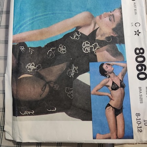 May include: A vintage sewing pattern for a swimsuit with a halter top and a matching bottom. The pattern is for sizes 8-10-12 and is from the 1980s. The pattern is printed on white paper with black ink and features a black and white illustration of a woman wearing the swimsuit.