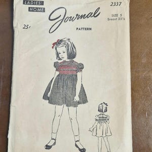 Può includere: Busta di cartamodello vintage di Ladies' Home Journal. L'illustrazione mostra una bambina in un vestito con un fiocco rosso. La busta riporta la scritta "Journal Pattern" e "Size 5 Breast 23 1/2". Il prezzo è di 25¢.