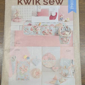 Peut inclure: Une couverture de patron de couture avec le logo "kwik sew" et le texte "SEWING ROOM ACCESSORIES". La couverture présente divers accessoires de couture, dont une machine à coudre, des contenants de rangement et des échantillons de tissu à motifs floraux.