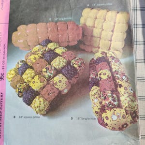 May include: Vintage sewing pattern featuring four quilted pillow and bolster designs. Includes a 14-inch square pillow, a 16-inch long bolster, and two other similar designs. The pattern shows various floral and geometric fabric patterns.
