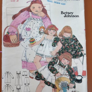 Può includere: Una busta per cartamodello Betsey Johnson taglia 3, con illustrazioni di bambini che indossano vari abiti e completi con motivi floreali e a quadretti, inclusi disegni tecnici dei capi nella parte inferiore della pagina.