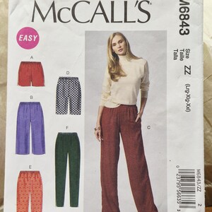 May include: McCall's M6843 sewing pattern envelope featuring illustrations of various pant styles including shorts, cropped pants, and full-length trousers in red, purple, green, and patterned fabrics, with a model wearing red patterned trousers.