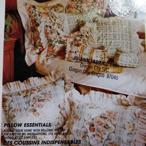 Può includere: Una collezione di cuscini decorativi con motivi floreali e bordi arruffati. I cuscini sono disposti su un letto, mostrando varie dimensioni e design. L'immagine include il testo "Pillow Essentials" e "Des Coussins Indispensables".