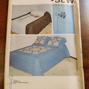 Pode incluir: Um envelope de padrão Kwik Sew vintage com ilustrações de conjuntos de cama. O envelope mostra um edredom azul com detalhes florais, uma colcha marrom e uma cortina de chuveiro floral. O texto "KWIK SEW" é exibido de forma proeminente.