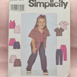 May include: A Simplicity sewing pattern envelope, featuring a young girl modeling clothing. The envelope includes illustrations of various tops, shorts, and pants. The pattern number is 8716, and the size is BB 5,6,7,8.