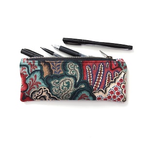 May include: A colorful floral patterned pencil case with a zipper closure. The case is filled with black pens.