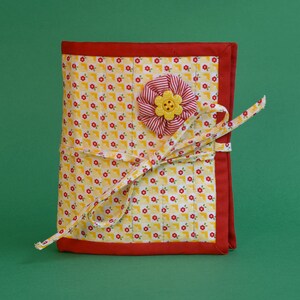 May include: A yellow and red fabric notebook with a red border and a yellow flower with a red center.