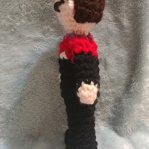 May include: A crocheted doll with brown hair, a red and black striped shirt, and black pants.