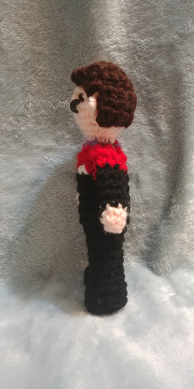 May include: A crocheted doll with brown hair, a red and black striped shirt, and black pants.