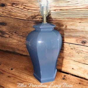 May include: A blue porcelain lamp base with a brass fitting and a clear glass lamp shade. The base has a geometric design and the text "Blue Porcelain Lamp Base" is written on the wooden surface.