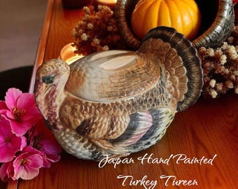 May include: A hand-painted ceramic turkey tureen with a lid, featuring brown, tan, and pink hues. The tureen is set on a wooden surface with candles and a cornucopia filled with a small pumpkin. Text on the image reads "Japan Hand Painted Turkey Tureen."