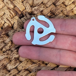 May include: A silver metal charm shaped like a vintage record adapter. The charm has a hole at the top for attaching to a necklace or keychain.