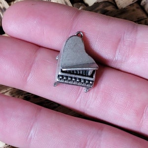 Peut inclure: Un charme en argent en forme de piano à queue. Le charme est détaillé avec des touches et un couvercle.
