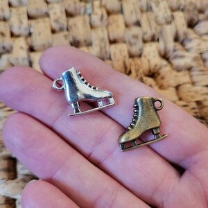 May include: Two silver ice skate charms, one with a silver finish and one with a bronze finish. The charms are in the shape of ice skates with laces and blades.